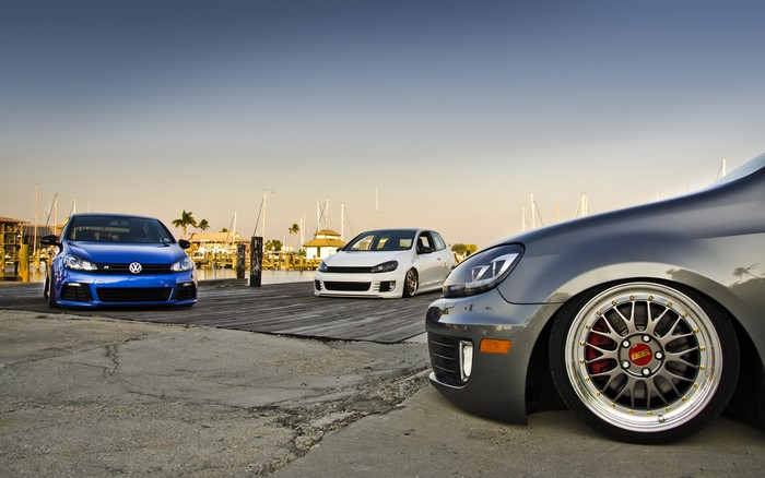 Three Volkswagen Golf cars parked by a marina