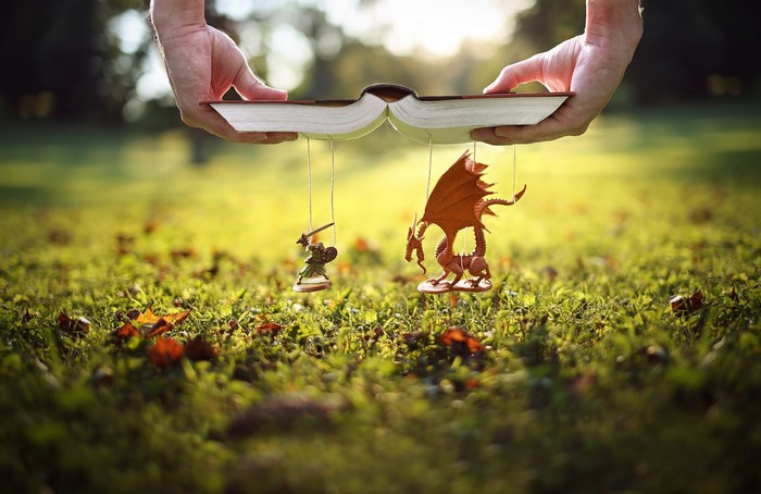 Hands holding a book with a dragon and warrior toy