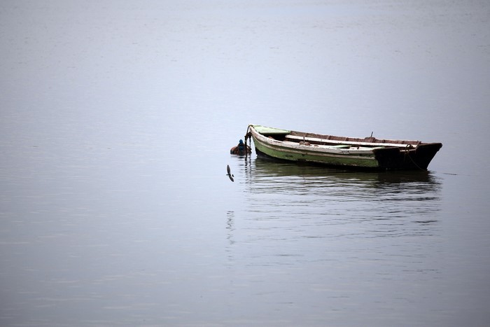 A lone green and white boat floats on calm water