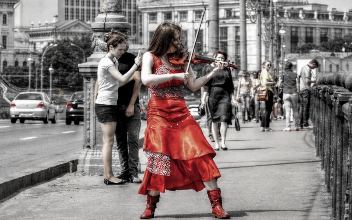 Woman playing violin on a street with people and cars