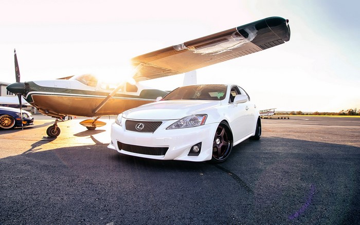 White Lexus IS parked next to a small airplane