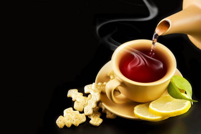 Tea being poured into a cup with lemons and cookies