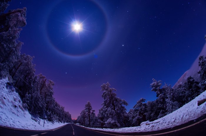 Moon halo over snowy road at night