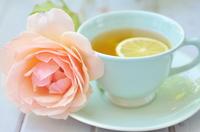 Close-up of a peach rose next to a cup of tea with lemon