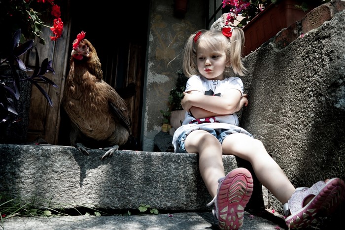 Little Girl Sitting with Chicken on Stone Steps