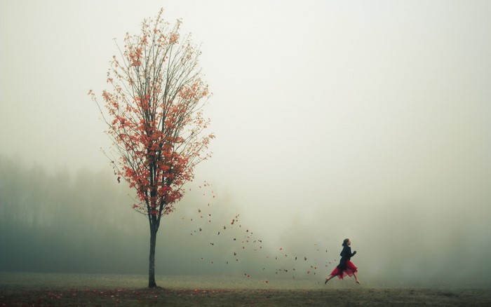 Woman running past a tree in autumn fog