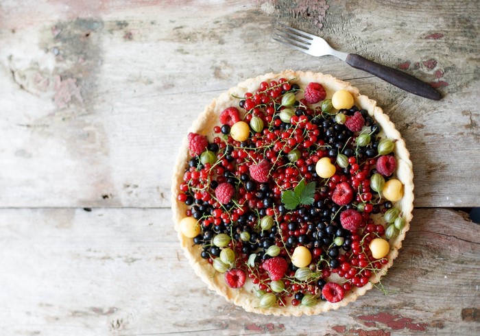 Fruit tart with raspberries, currants, and gooseberries on a wooden table