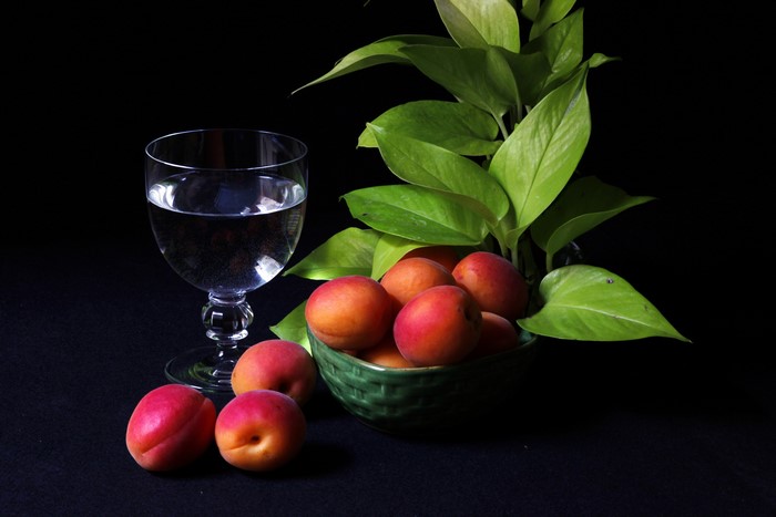 Apricots in a bowl with a glass of water and plant