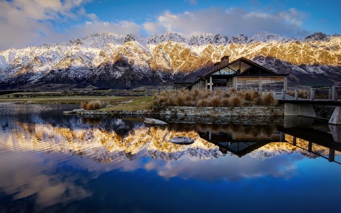 Modern house reflecting on a lake with snow-capped mountains