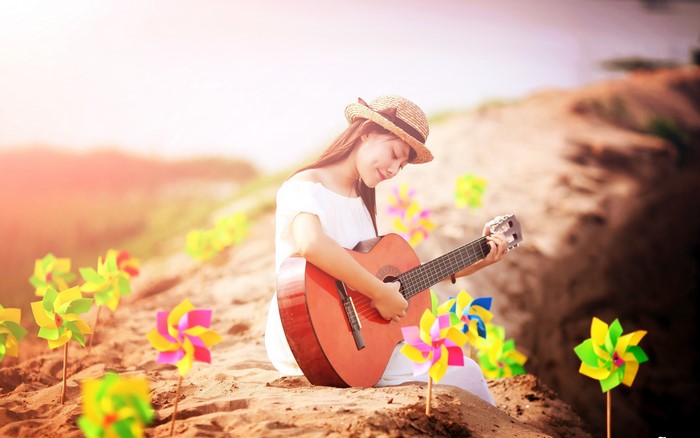 Asian girl playing guitar on a sandy hill with pinwheels