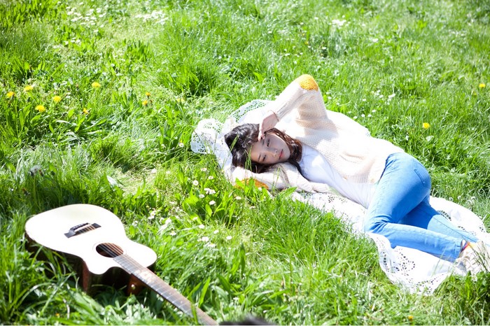 Asian woman lying on grass with guitar