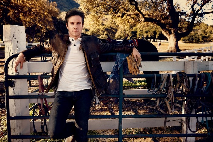 Armie Hammer leaning on a fence with horse tack