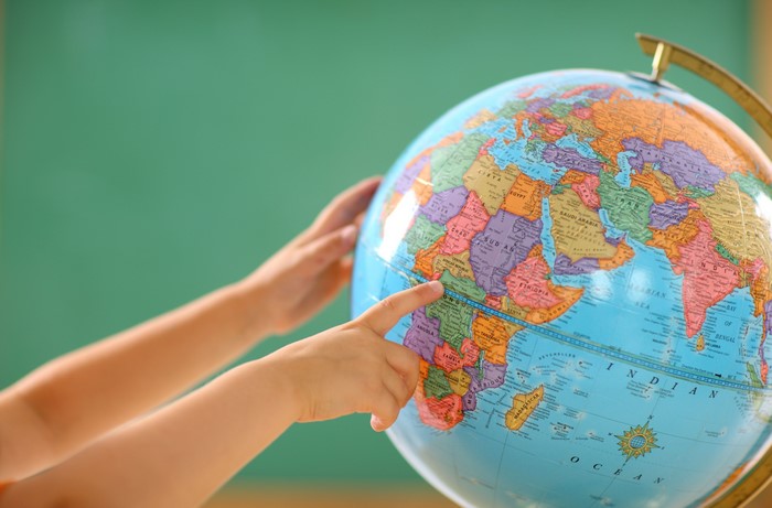 Children's hands pointing at a globe