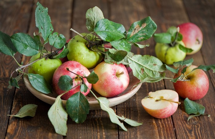 Apples with leaves in a bowl on a wooden table