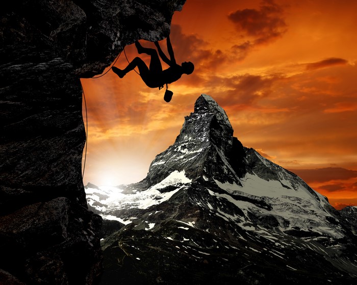 Rock climber silhouetted against sunset over mountains