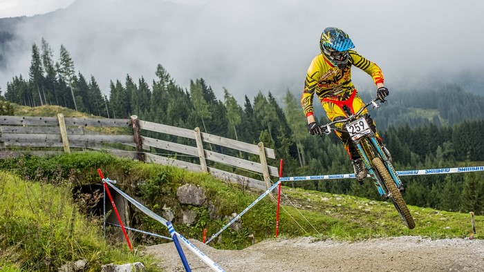 Downhill mountain biker in yellow and red gear jumps over a track