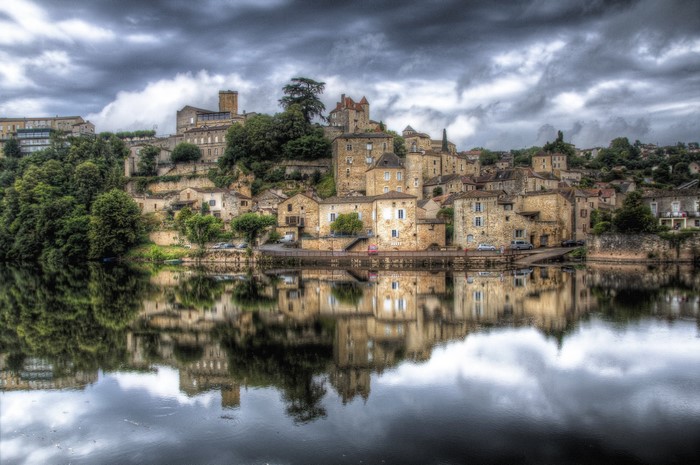 Puy l'Eveque village reflected in a river under a cloudy sky