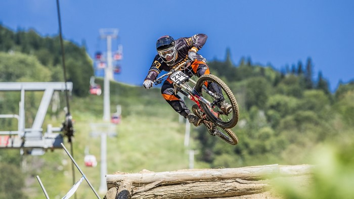 Downhill mountain biker jumping over a log obstacle