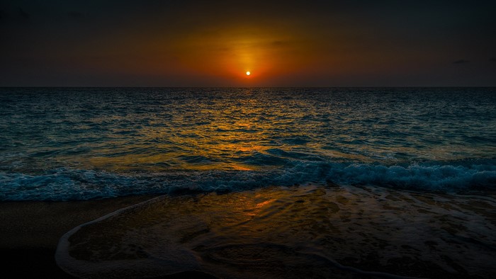 Sunset over the ocean with waves crashing on the shore
