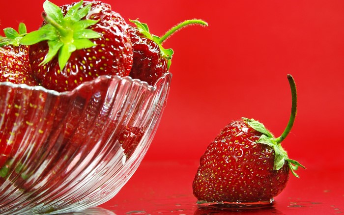 Strawberries in a glass bowl and on a red surface