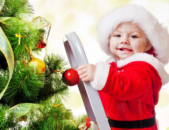 Baby in Santa costume decorating a Christmas tree
