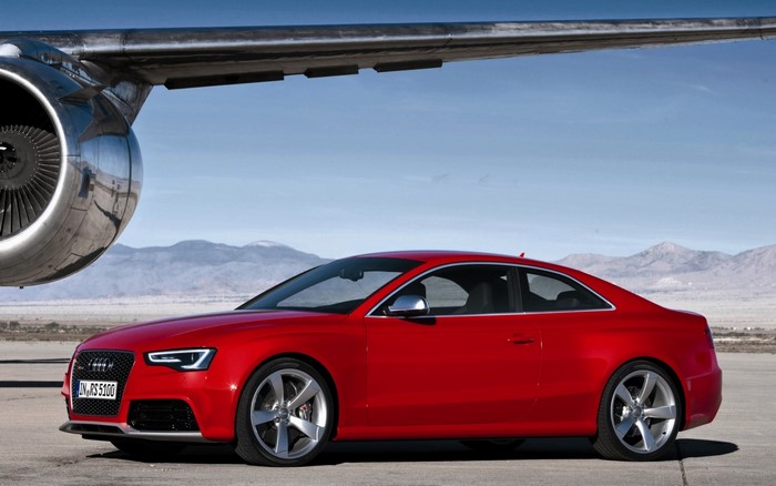 Red Audi RS5 parked next to an airplane engine