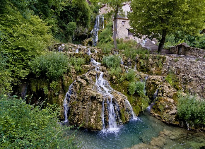 Waterfalls cascading down mossy rocks near a stone building in Burgos, Spain
