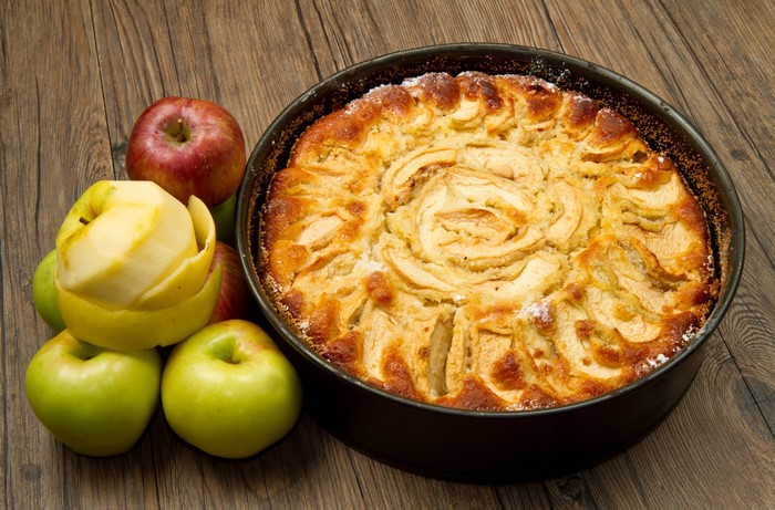 Apple pie with fresh apples on a wooden table