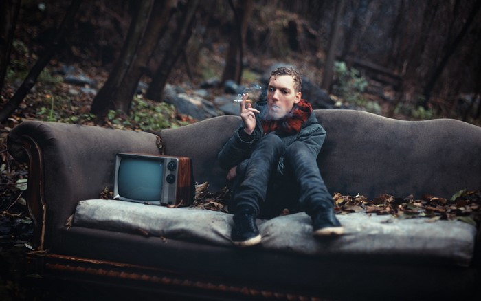 Man smoking on a sofa with a TV in the woods
