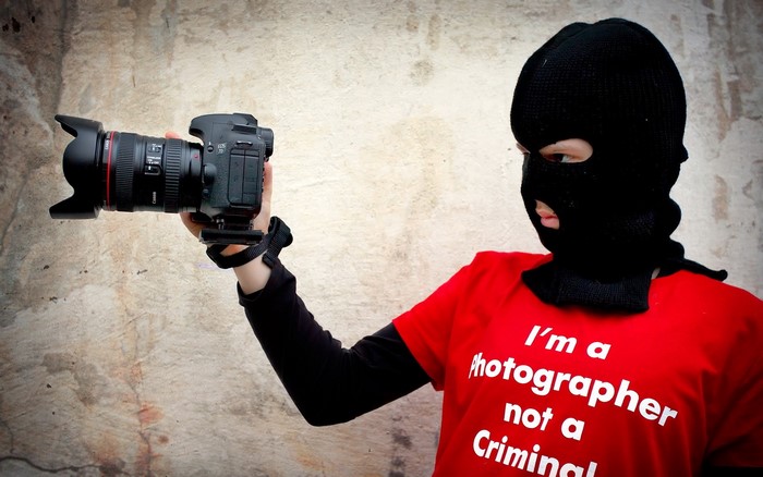 Person in ski mask holding a Canon camera