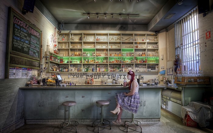 Woman sitting at a bar with bottles on shelves