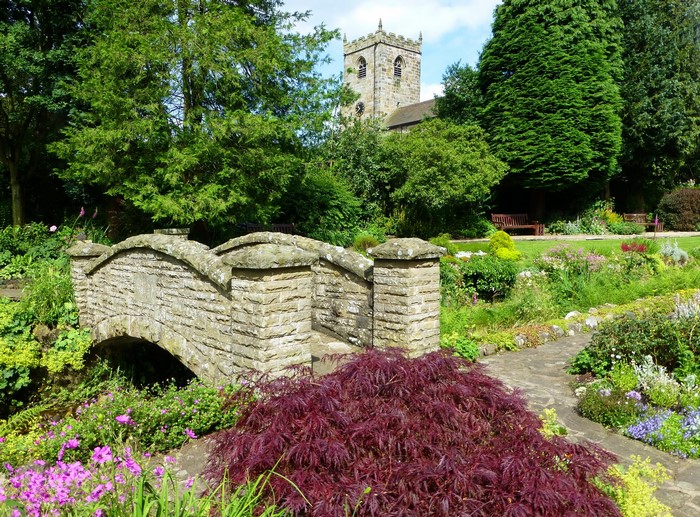 Stone bridge in a park with a church tower in Waddington, England