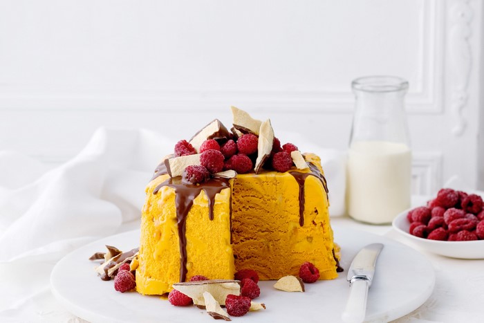 Yellow ice cream cake with raspberries and chocolate drizzle