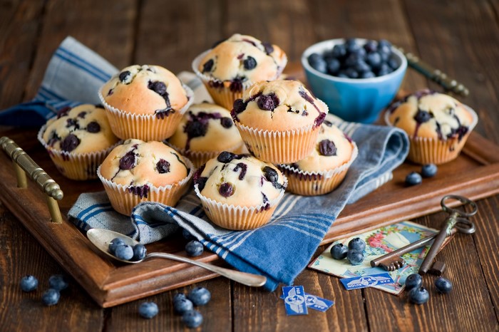 Blueberry muffins on a wooden tray with blueberries