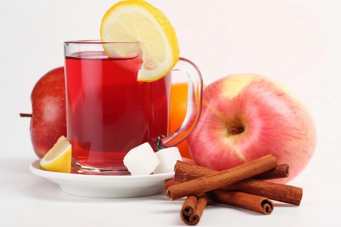 Red drink in a mug with apples, lemon, cinnamon, and sugar cubes