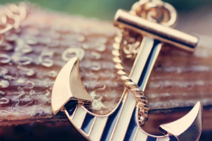 Close-up of a gold anchor pendant with blue and white stripes