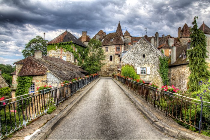 Stone bridge leading to a French village with old buildings