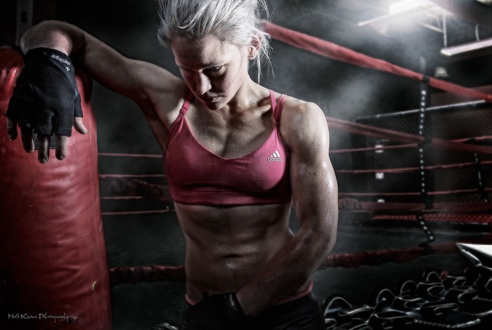 Female boxer leaning on punching bag in boxing ring