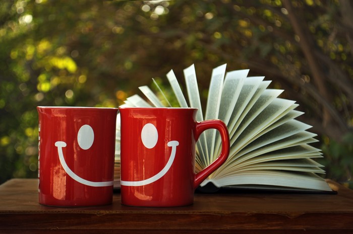 Two red mugs with smiley faces and an open book