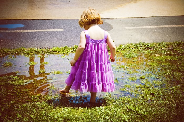 Little girl in purple dress playing in a puddle