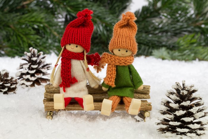 Two dolls in winter hats and scarves sitting on a log bench