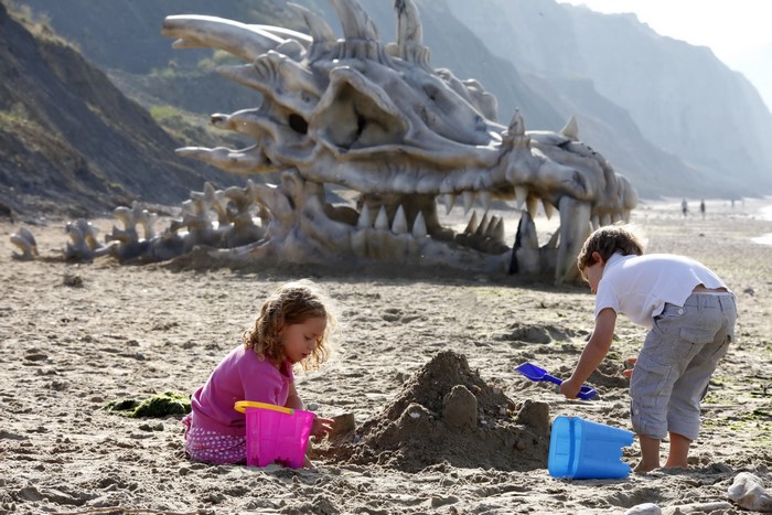 Children playing on a beach with a dragon skeleton