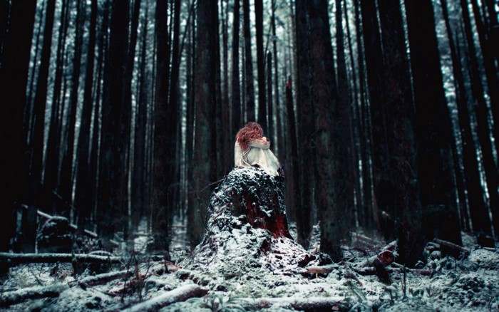 Girl sitting on a snow-covered tree stump in a dark forest