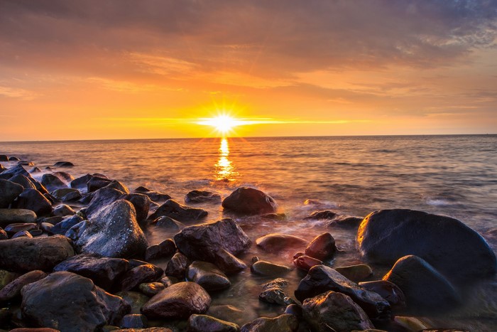 Sunset over the sea with rocks on the shore