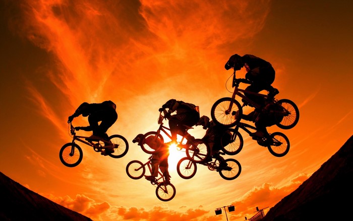 BMX riders performing jumps against a sunset sky