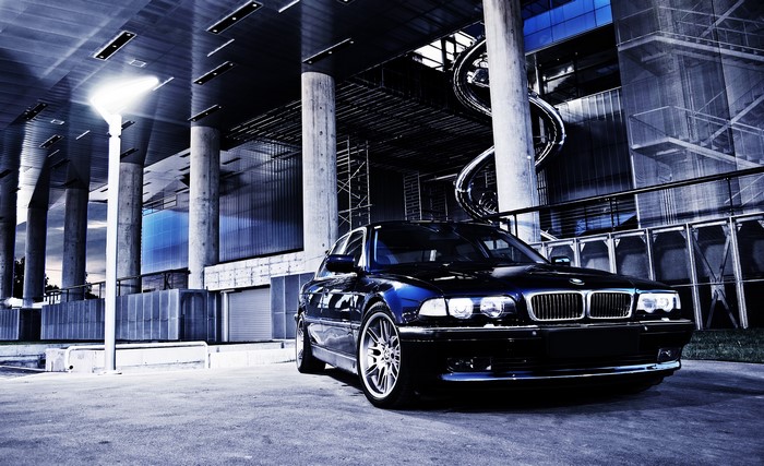 Black BMW 740i E38 parked in front of modern architecture