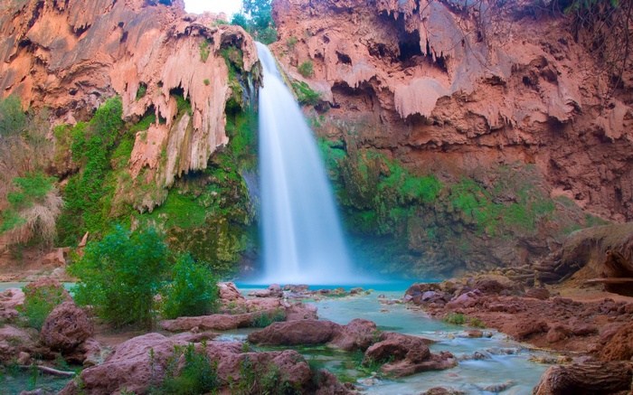 Waterfall cascading into a turquoise pool surrounded by red rocks and greenery