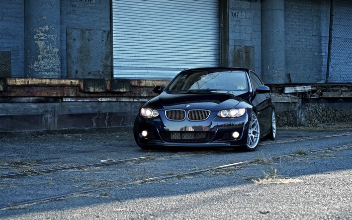 Black BMW parked on train tracks near industrial building