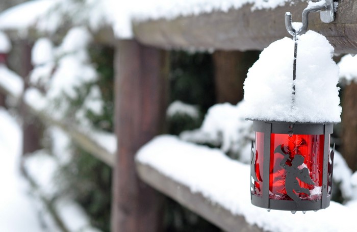 Snow covered lantern hanging on a wooden fence