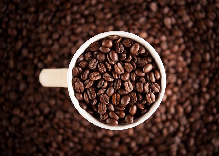 A white mug filled with coffee beans on a background of coffee beans